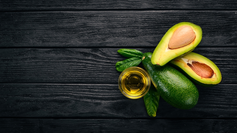 Avocado and avocado oil on a wooden background. Top view. Free space for your text.