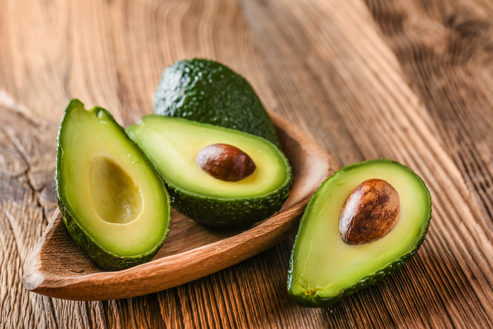 Avocado on old wooden table.Halfs on wooden bowl. Fruits healthy food concept.
