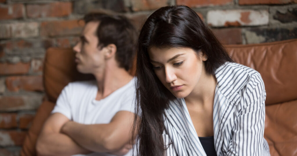 Sad pensive young girl thinking of relationships problems sitting on sofa with offended boyfriend, conflicts in marriage, upset couple after fight dispute, making decision of breaking up get divorced