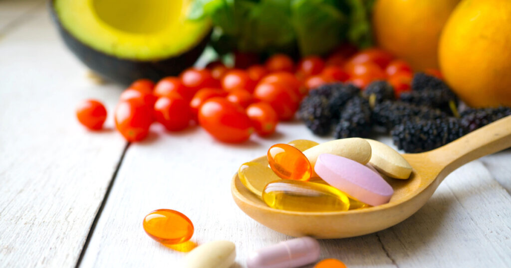 Pills and capsules in wooden spoon with fresh fruits.Multivitamins and supplement from fruits concept.