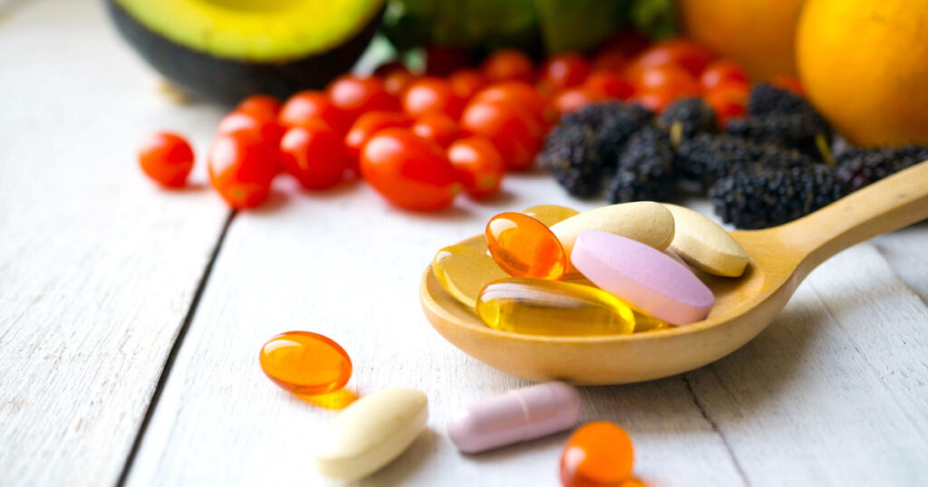 Pills and capsules in wooden spoon with fresh fruits.Multivitamins and supplement from fruits concept.
