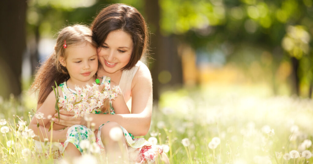 Happy mother and daughter in the park. Beauty nature scene with family outdoor lifestyle. Happy family resting together on the green grass, having fun outdoor. Happiness and harmony in family life.