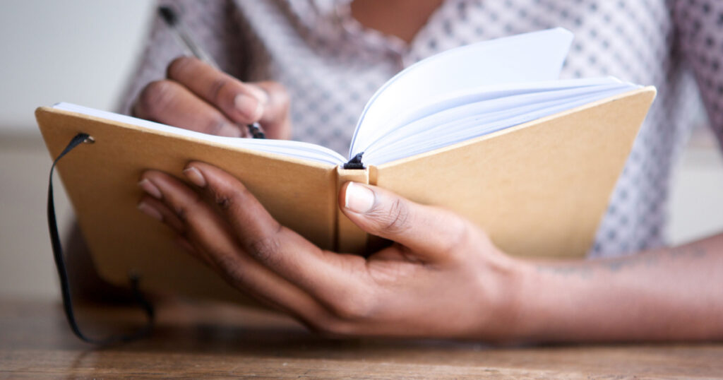 Close up partial portrait of black female author at home writing in journal