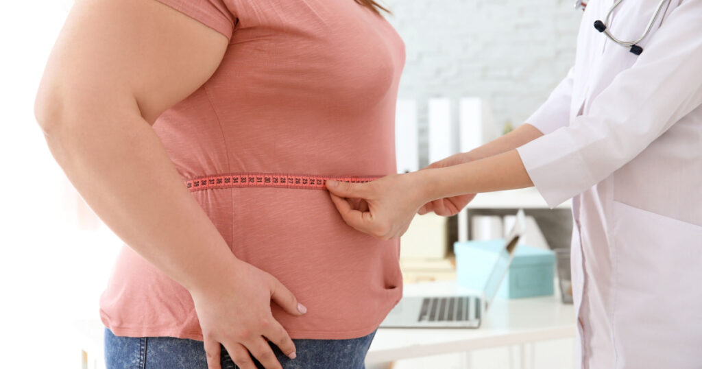 Female doctor measuring waist of overweight woman with measuring tape in clinic