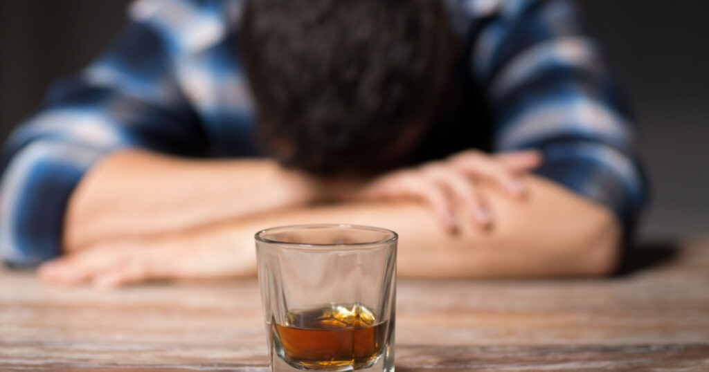 alcoholism, alcohol addiction and people concept - male alcoholic with glass of whiskey lying or sleeping on table at night