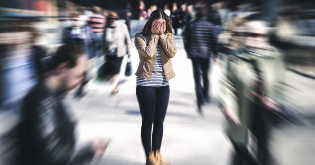 Panic attack in public place. Woman having panic disorder in city. Psychology, solitude, fear or mental health problems concept. Depressed sad person surrounded by people walking in busy street.