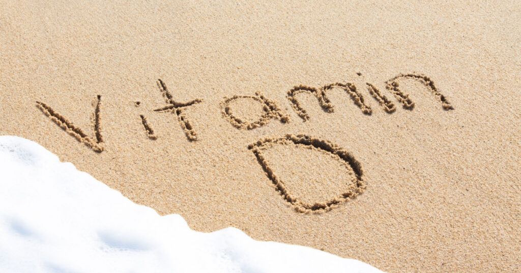 Vitamin D written in the sand with foam from a wave washing up