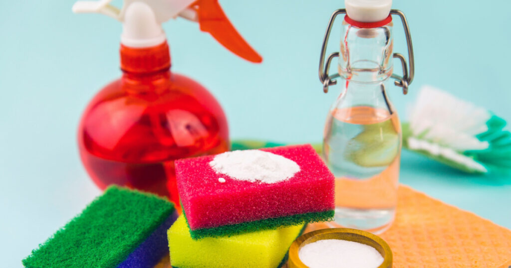 Nature and eco friendly homemade natural cleaners baking soda, white vinegar in vintage bottle, washing sponges for cleaning home, non toxic cleaning products, isolated on blue background.