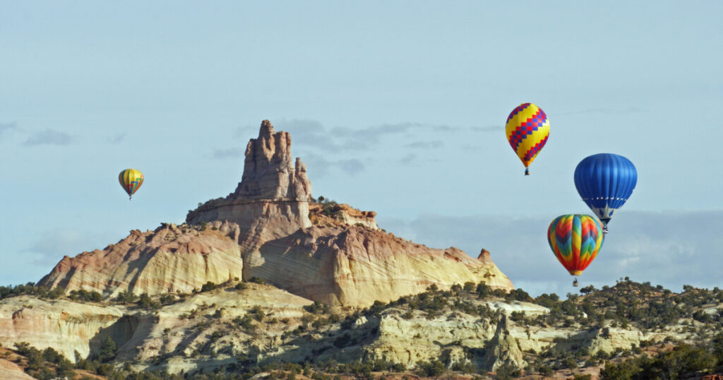 A group of hot air balloons rise above the red sandstone of Red Rocks State Park near Gallup, New Mexico, and circle around the Church Rock formation