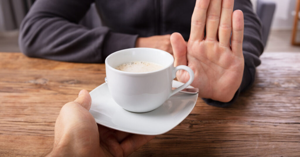 Close-up Of A Man's Hand Refusing Cup Of Coffee Offered By Person Over Wooden Desk