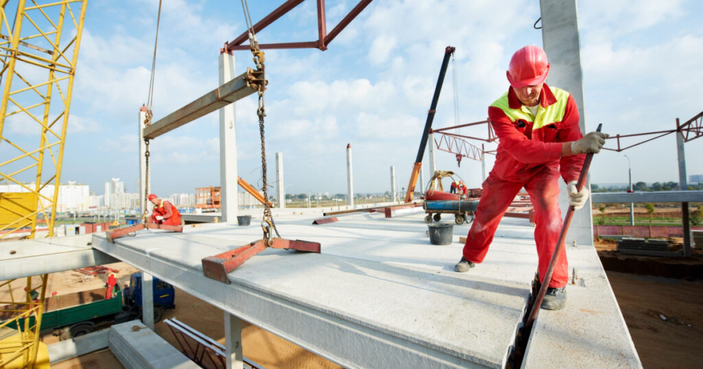 builder worker in safety protective equipment installing concrete floor slab panel at building construction site