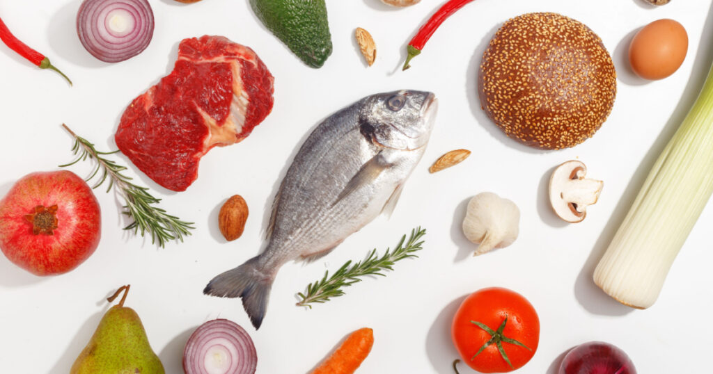 Healthy food clean eating selection: fruit, vegetable, seeds, fish, meat, leaf vegetable on white background. Top view.