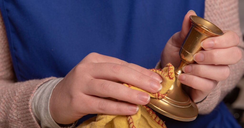 woman cleaning brass candle sticks with a yellow duster