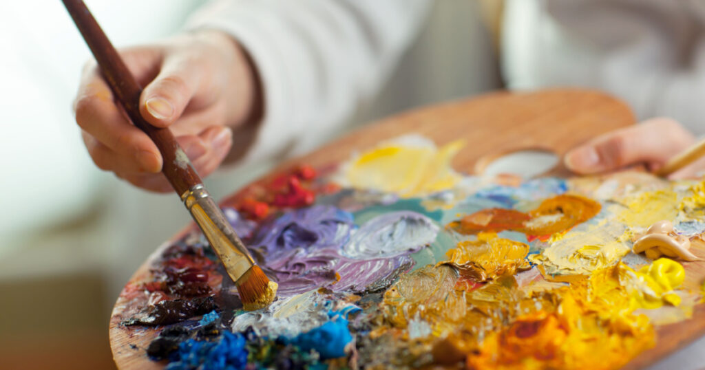 artist brush mix color oil painting on palette is holding in his hand closeup