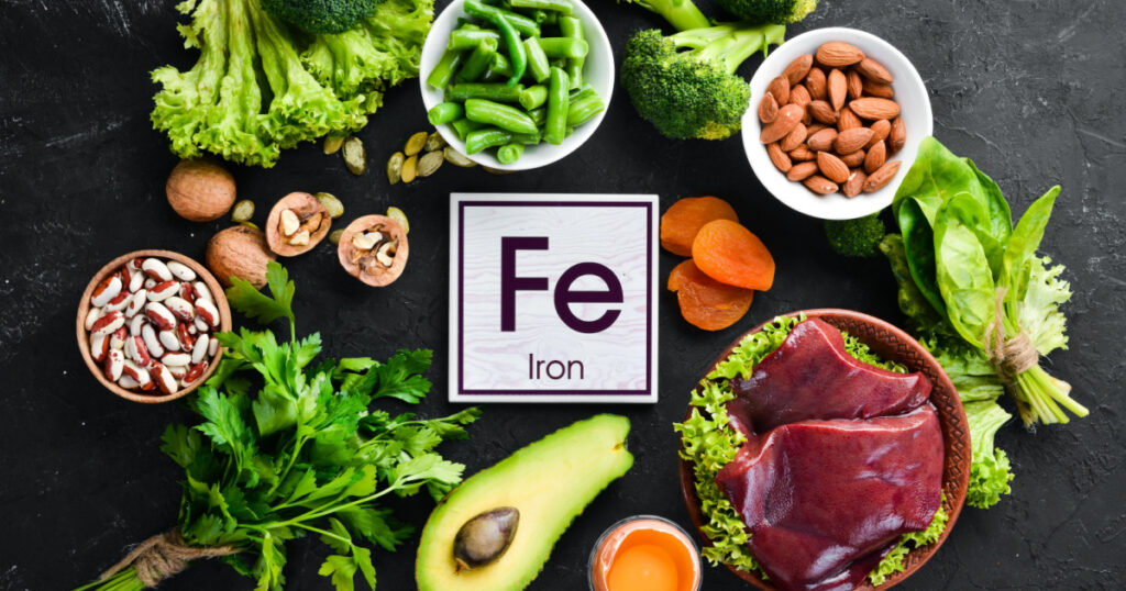 Food containing natural iron. Fe: Liver, avocado, broccoli, spinach, parsley, beans, nuts, on a black stone background. Top view.