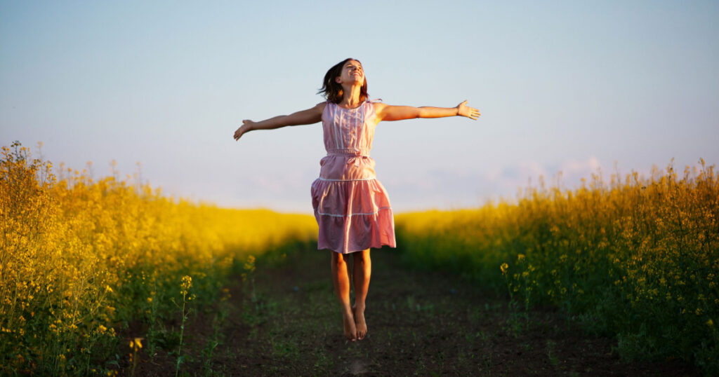 Happy woman jumps to the sky in the yellow meadow at the sunset