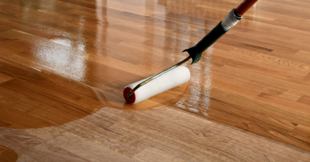 Lacquering wood floors. Worker uses a roller to coating floors. Varnishing lacquering parquet floor by paint roller - second layer. Home renovation parquet