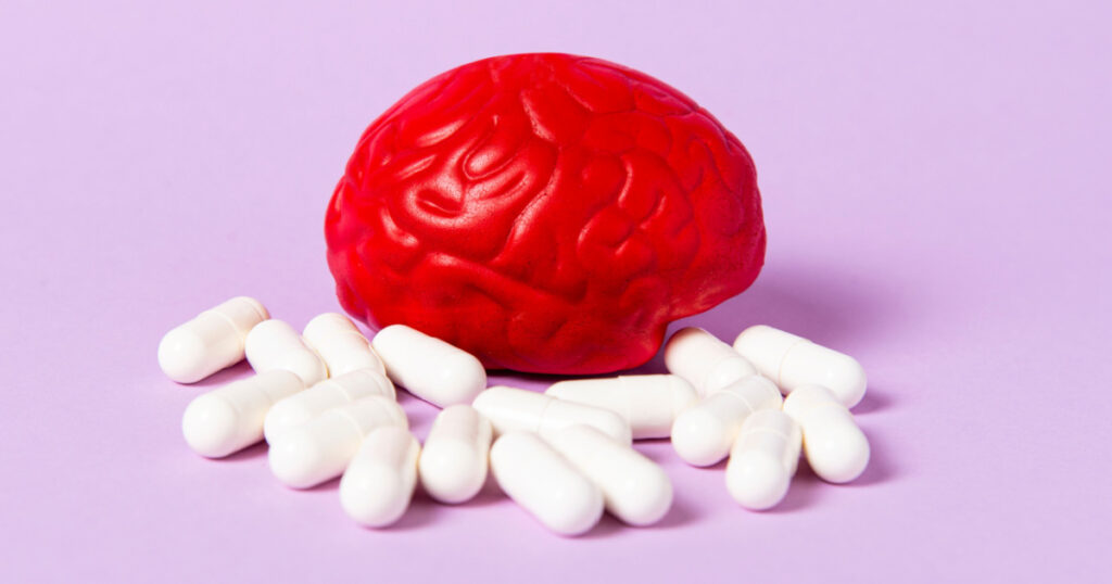 Red brain on a pink background with white pills. Some pills for the brain. Symbolic for drugs, psychopharmaceuticals, nootropics and other drugs. The medicine. Brain treatment