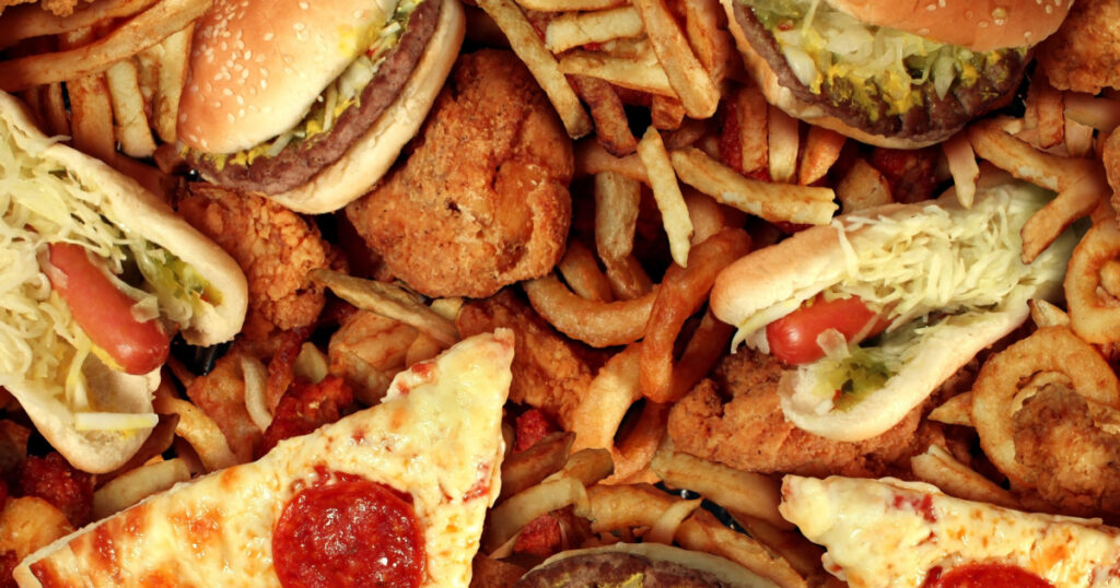 Fast food concept with greasy fried restaurant take out as onion rings burger and hot dogs with fried chicken french fries and pizza as a symbol of diet temptation resulting in unhealthy nutrition.