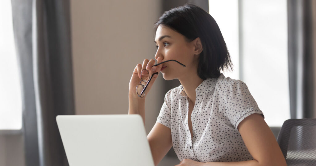 Thoughtful anxious asian business woman looking away thinking solving problem at work, worried serious young chinese woman concerned make difficult decision lost in thought reflecting sit with laptop