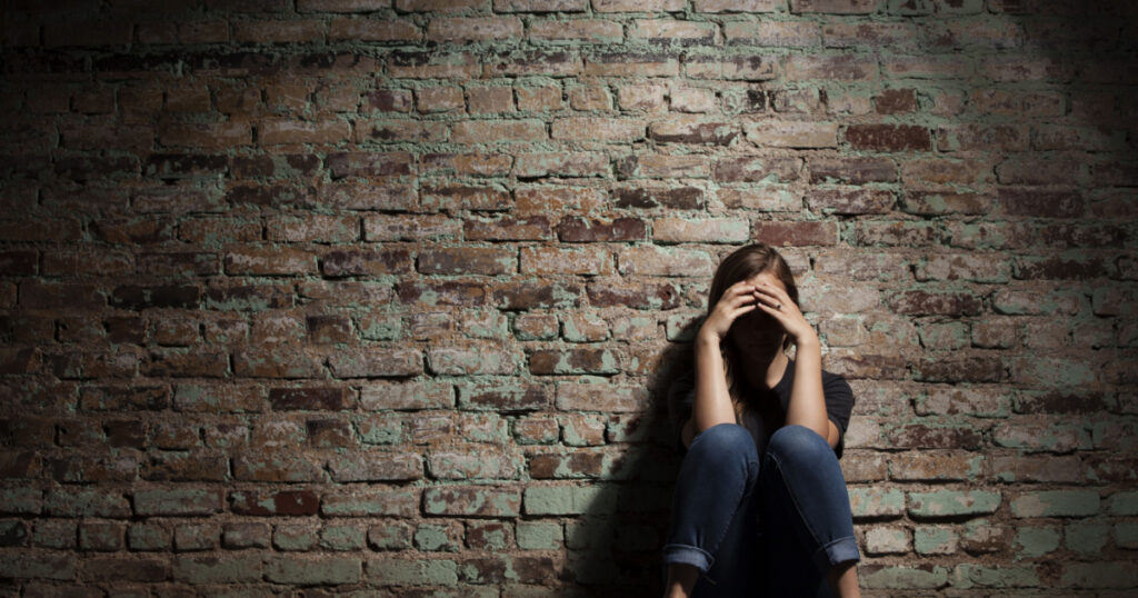 Sad woman sitting alone against brick wall.