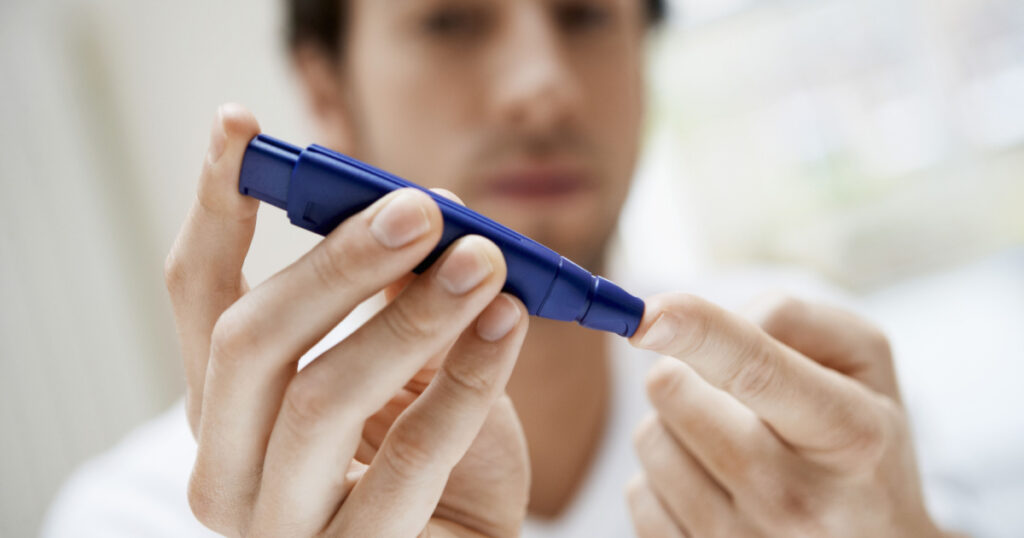 Closeup of young man using lancelet on finger in bathroom