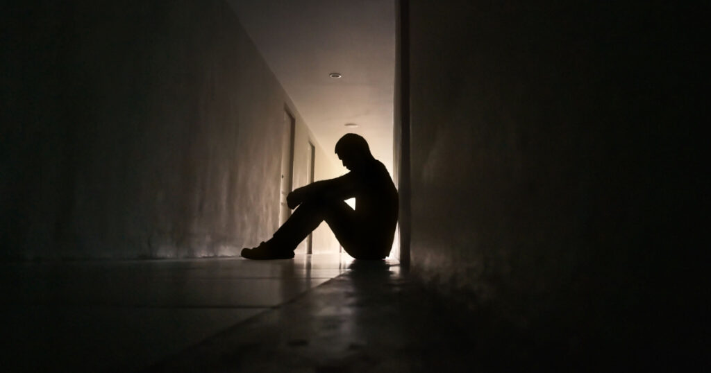 Silhouette of depressed man sitting on walkway of residence building. Sad man, Cry, drama, lonely and unhappy concept.