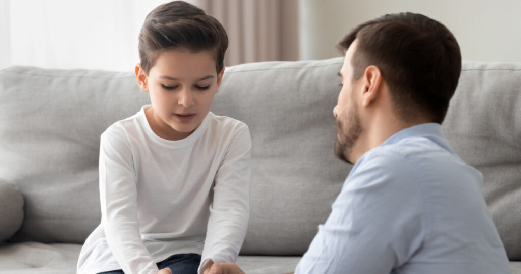 Worried loving young single father holding hand talking comforting upset little kid son sharing helping with problem, caring dad foster parent give support apologizing supporting listening child boy