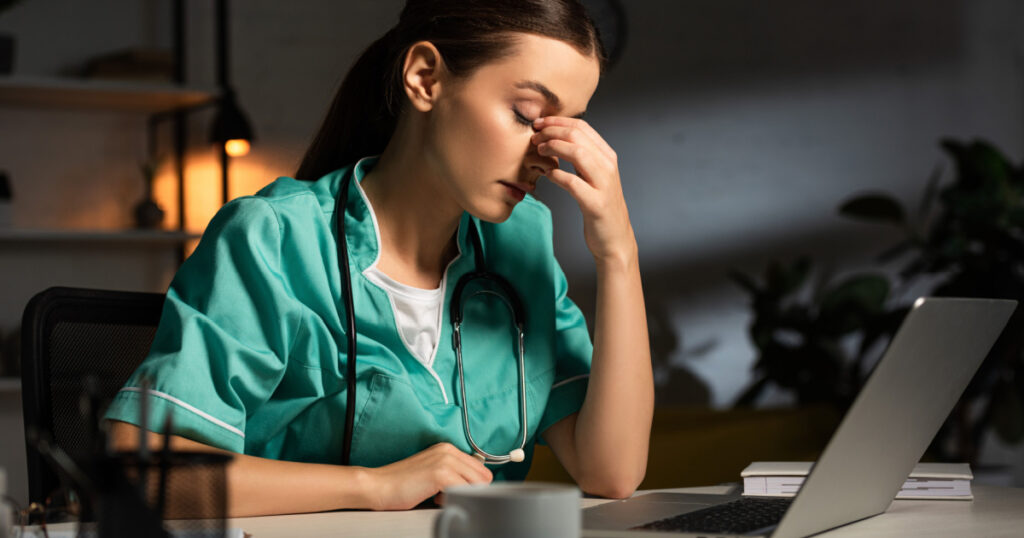 attractive and tired nurse in uniform sitting at table during night shift