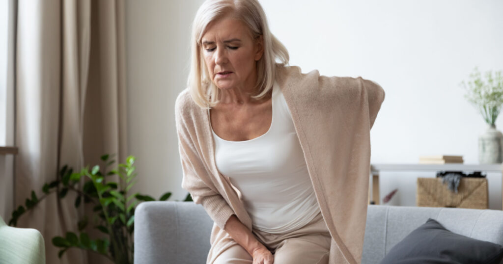 Elderly 60s woman got up from couch felt severe painful feelings in lumbar, massaging low back to reduce ache, suffer from backache discomfort, diseases of older people, sciatic nerve injury concept