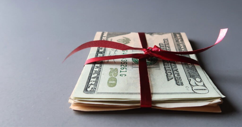 Cash dollar money in red ribbon on gray background with copy space - concept of money saving budget for holiday season on bonus money gift for someone