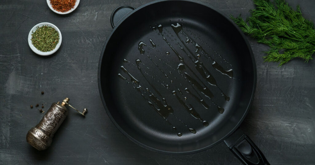 Man pouring cooking oil on the frying pan - Top View on a dark background
