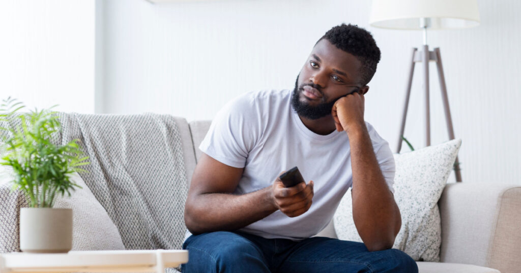 Bad tv program. Bored african guy sitting at home, switching tv for fascinating film, free space