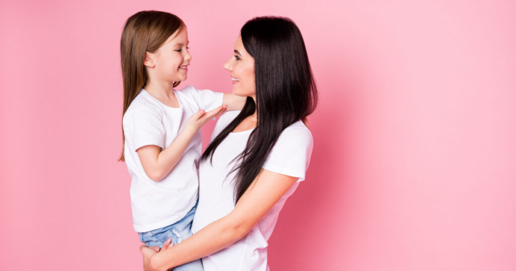 Portrait of two nice attractive lovely cute sweet careful cheerful cheery friendly sisters mom carrying daughter speaking contact growing up isolated over pink pastel color background