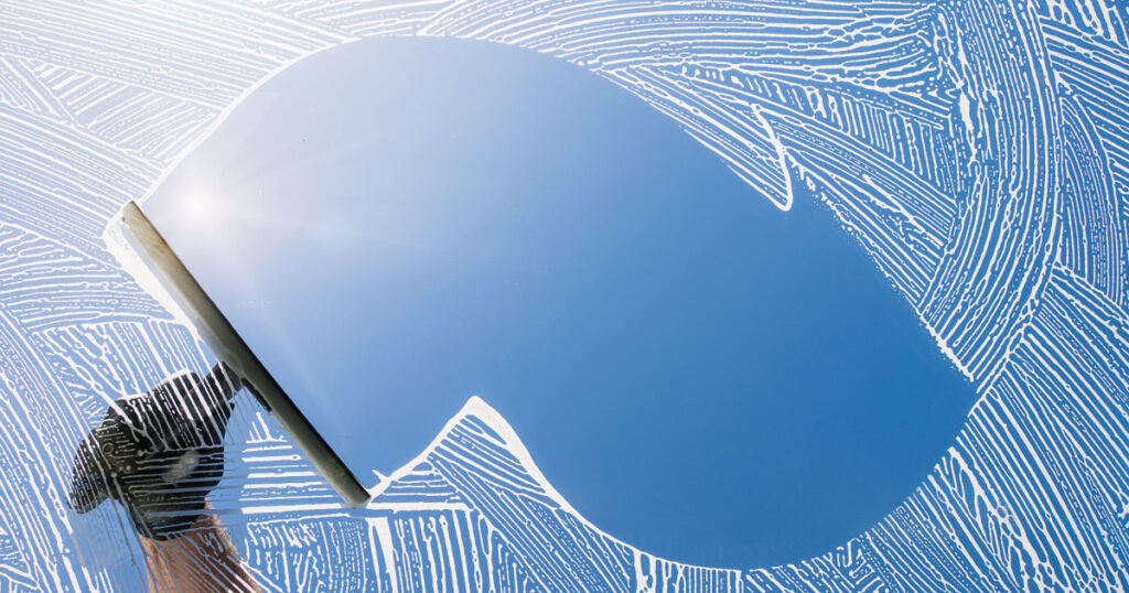 window cleaner cleaning window with squeegee and wiper on a sunny day