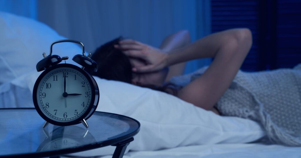 Unhappy woman with insomnia lying on bed next to alarm clock at night