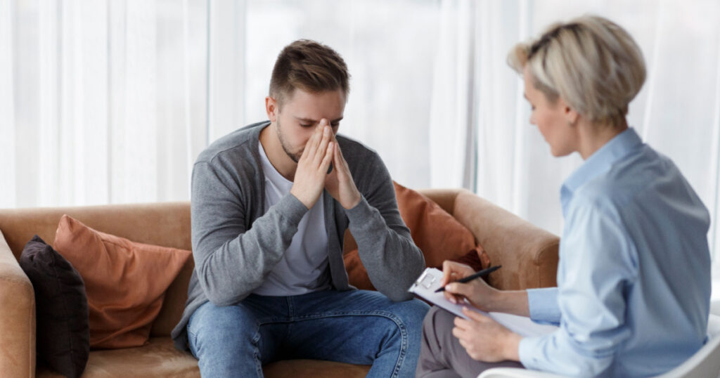 Depression Counseling. Desperate Man Telling About Unhappy Life While Professional Psychologist Taking Notes During Appointment In Office. Selective Focus