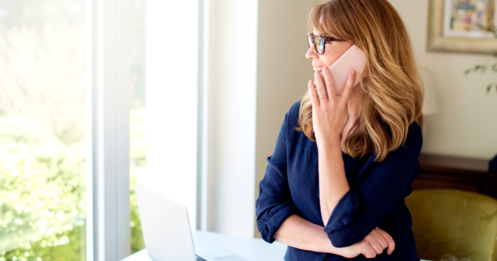 Portrait of middle aged woman using mobile phone and making a call while working from home. Home office.