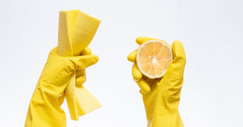 hands in yellow rubber gloves for cleaning hold a rag and lemon on a white background, natural cleaning products for home and kitchen, professional cleaning