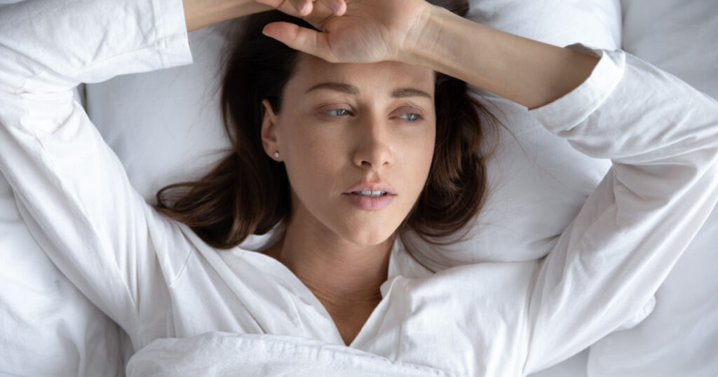 Top view of depressed sad young woman lie relax in bed look in distance thinking remembering, upset stressed millennial female rest in home bedroom feel sick suffer from illness or depression