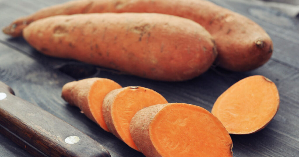 Raw sweet potatoes on wooden background closeup