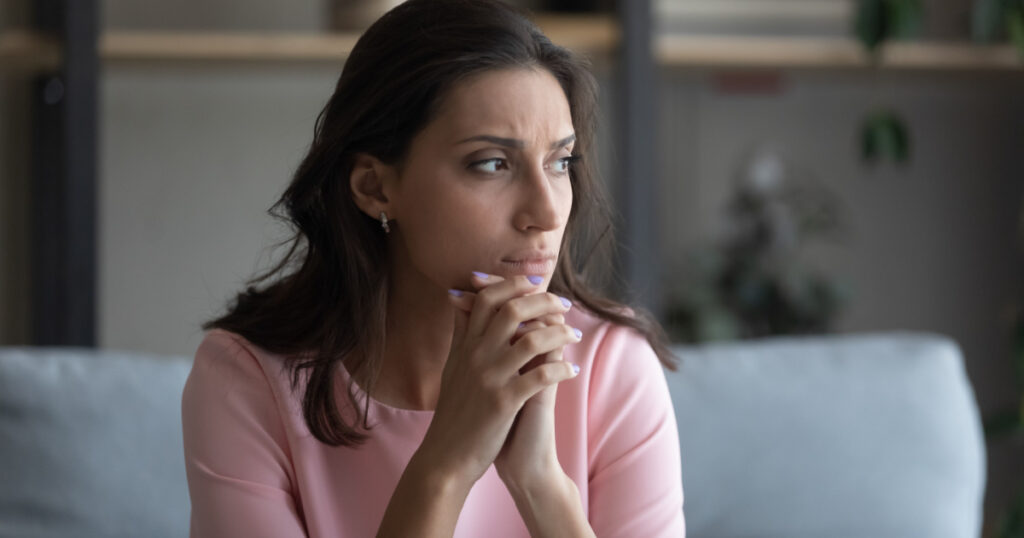 Worried young indian Arabic woman sit on couch at home look in distance thinking pondering, anxious unhappy arab mixed race female suffer from mental psychological personal problems, mourn or yearn