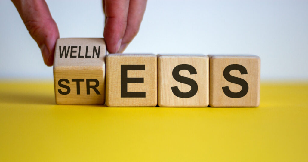 Wellness instead of stress. Hand turns a cube and changes the word 'stress' to 'wellness'. Beautiful yellow table, white background. Concept. Copy space.