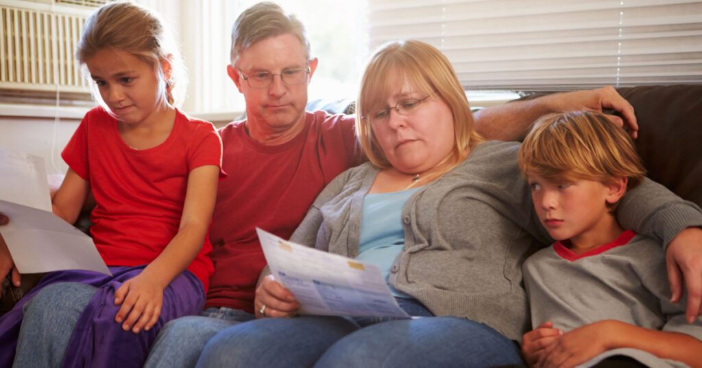 Unhappy Family Sitting On Sofa Looking At Bills
