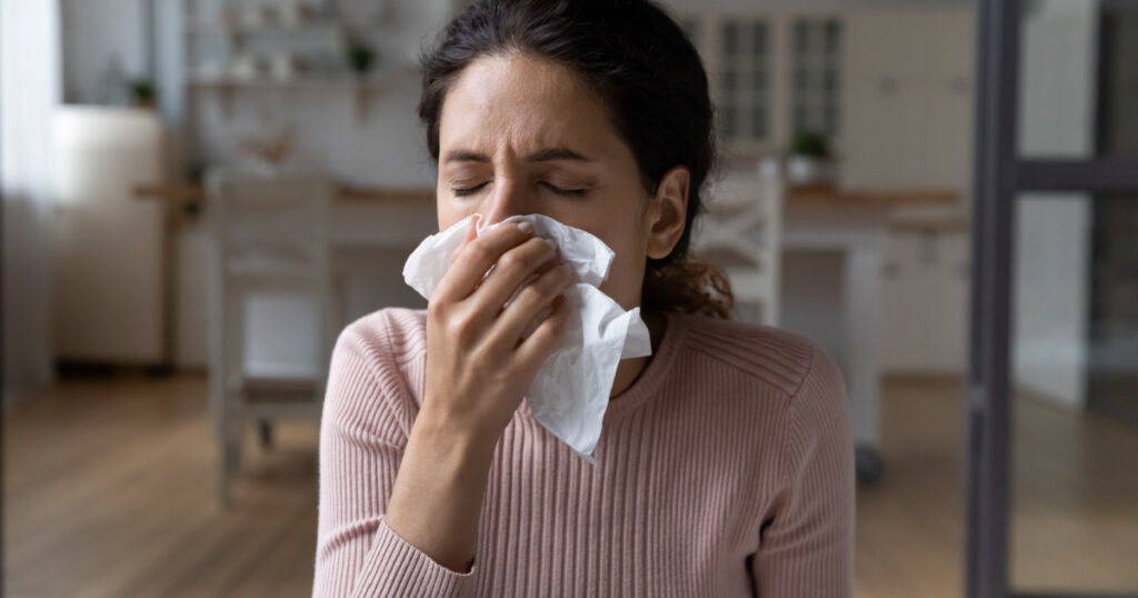 Running nose. Ill latina lady staying at home catching cold rhinitis viral bacterial infection using hygienic one time handkerchief. Young female suffer from seasonal allergy blow nose in paper tissue