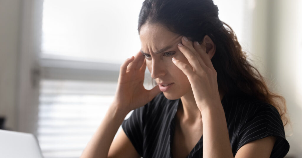 What should I do. Stressed latina woman sit by pc rub temples feel information overload unable to focus attention on work. Anxious young female try to remember important thing solve unexpected problem