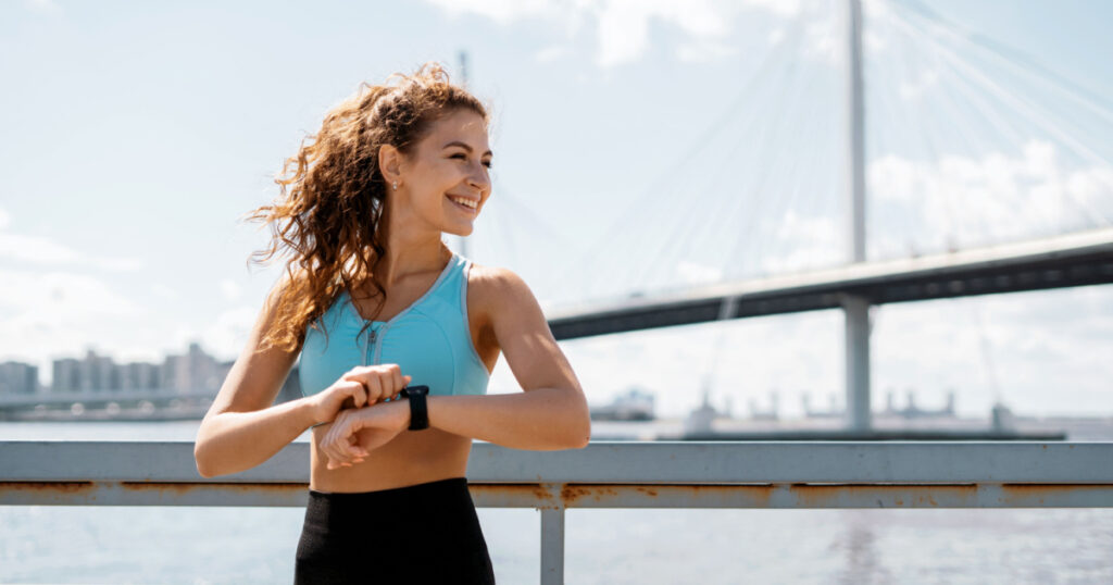 Uses a smart watch to measure the pulse on the hands. A woman does sports on the street. Fitness and a healthy lifestyle. The trainer does exercises for stretching the body.
