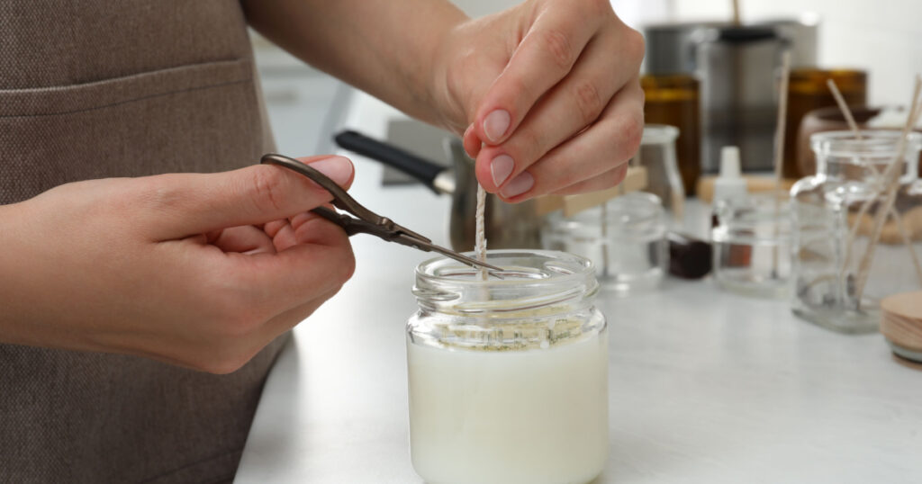 Woman cutting wick of homemade candle at table indoors, closeup