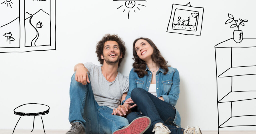 Portrait Of Happy Young Couple Sitting On Floor Looking Up While Dreaming Their New Home And Furnishing