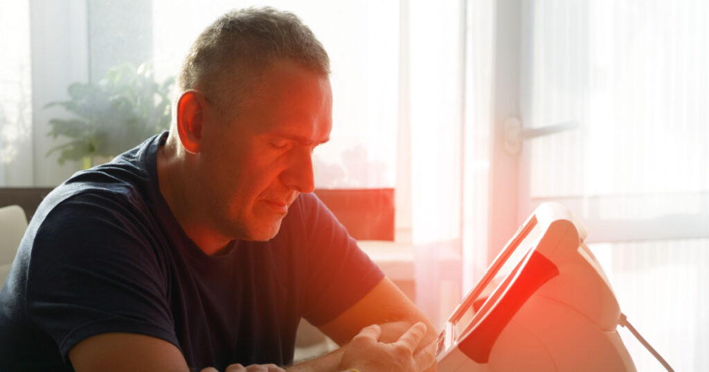 Man treating pain in the sinuses and head with infrared light therapy. The man sits at the table near the healing lamp.